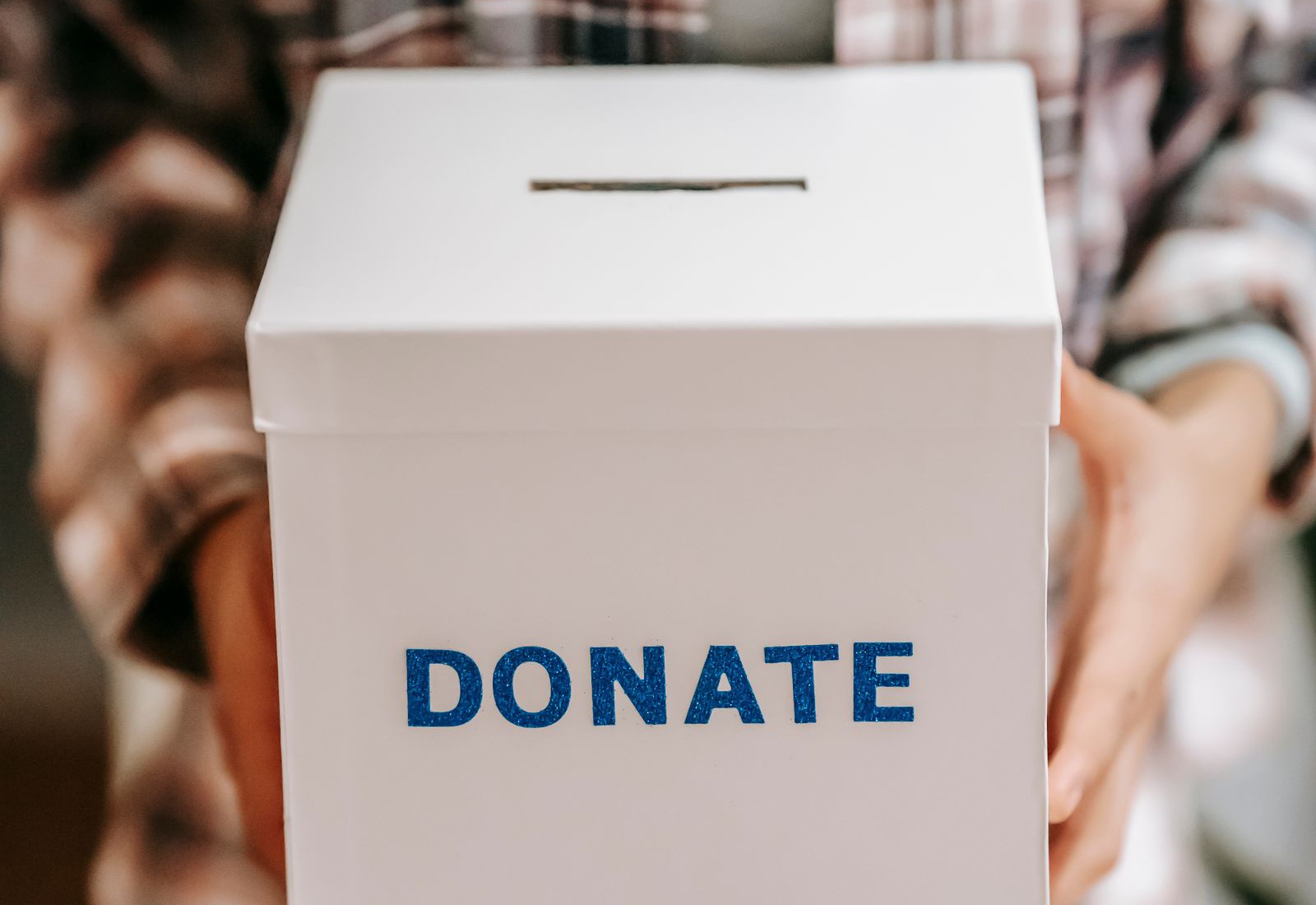 A person in a checked shirt holding out a white collection box with DONATE on the front in blue letters