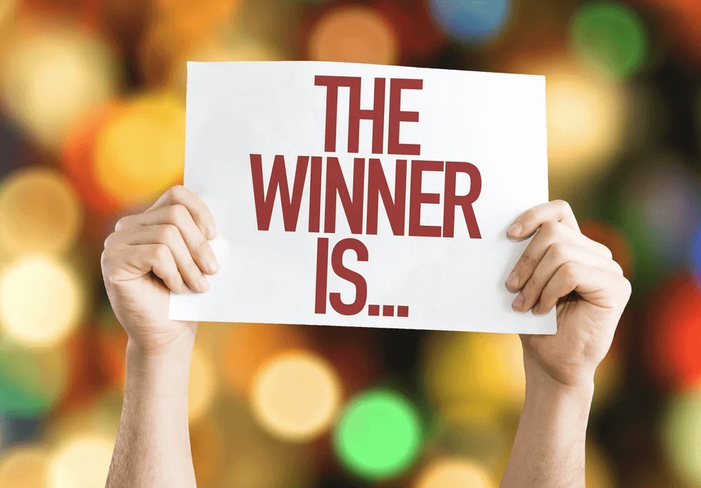 Hands holding up a sign reading "The winner is…" against festive bokeh lights