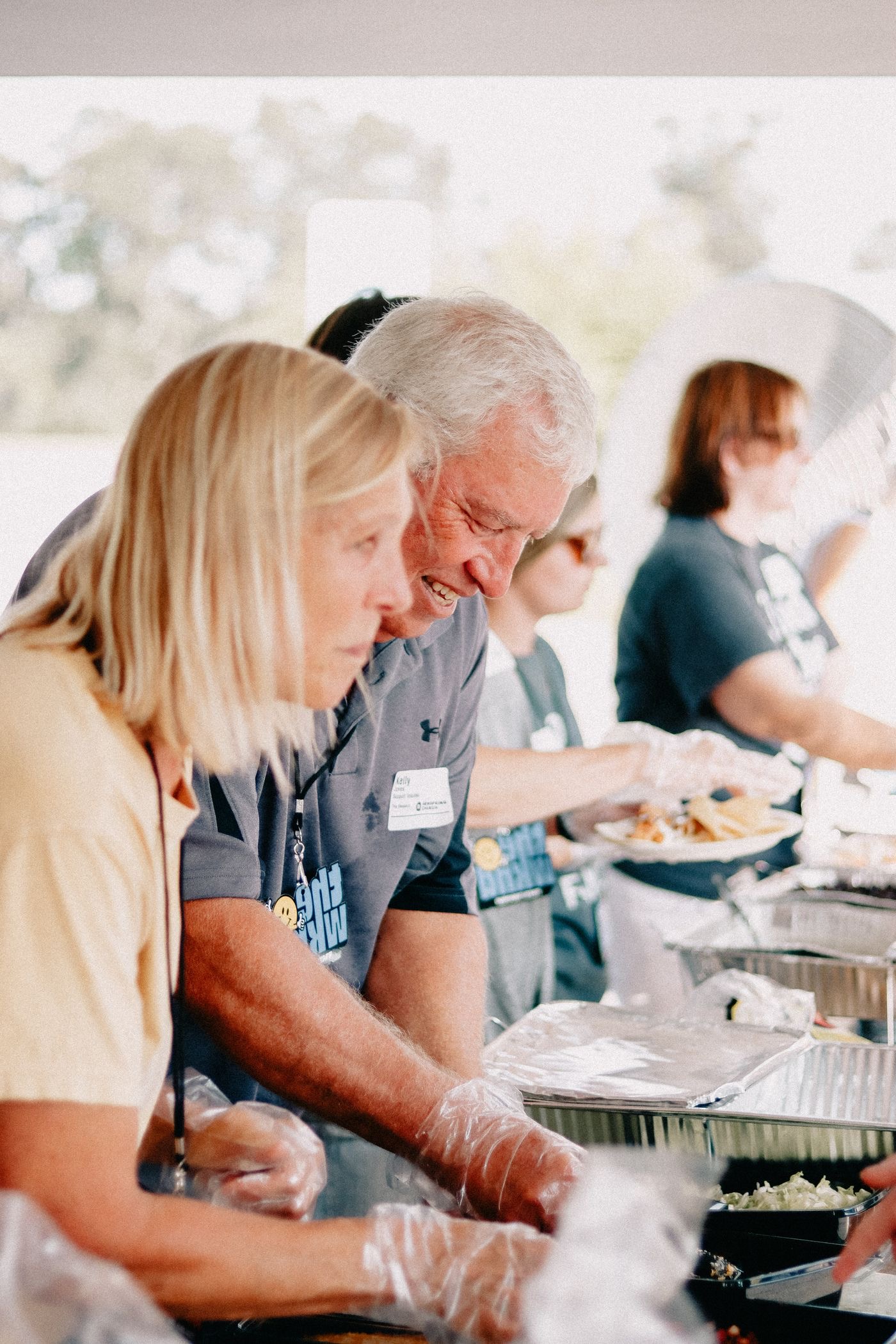 Volunteers in matching t-shirts serving food from trays at an outdoor community event