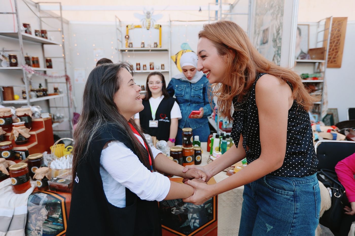 A volunteer at a community stall holding a visitor’s hands and laughing